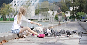 A beautiful child feeds pigeons bread at the lake in summer.