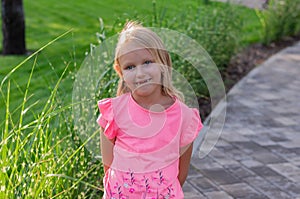 Beautiful child, a girl of 6-7 years old, a blonde with missing front teeth, standing in a park and smiling.