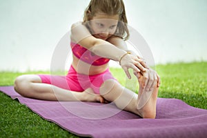 Beautiful child girl doing stretching exercises on yoga mat in sport uniform at backyard