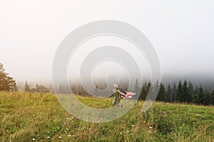 Beautiful child girl in hat with the American flag on foggy mountains. Independence Day of United States USA on 4th of