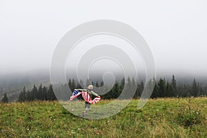 Beautiful child girl in hat with the American flag on foggy mountains. Independence Day of United States USA on 4th of