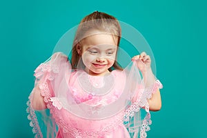 Beautiful child girl holding lace hem of her pink dress on blue isolated