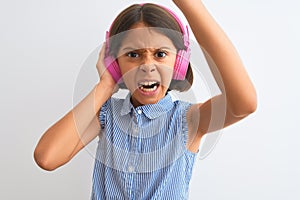 Beautiful child girl listening to music using headphones over isolated white background annoyed and frustrated shouting with