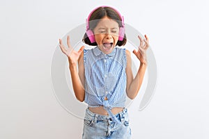 Beautiful child girl listening to music using headphones over isolated white background celebrating mad and crazy for success with