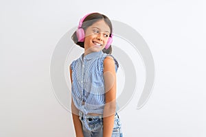 Beautiful child girl listening to music using headphones over isolated white background looking away to side with smile on face,