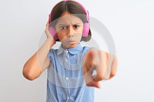 Beautiful child girl listening to music using headphones over isolated white background pointing with finger to the camera and to