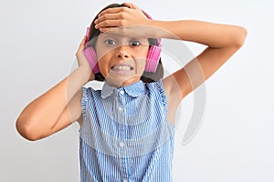 Beautiful child girl listening to music using headphones over isolated white background stressed with hand on head, shocked with