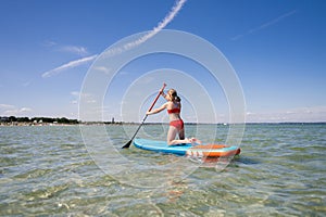 Beautiful child girl practice paddling on surfboard in sea at summer