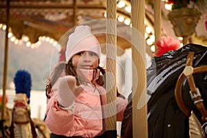 Beautiful child girl riding a merry go round carousel horse, enjoying happy time at Christmas funfair.