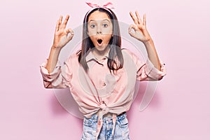 Beautiful child girl wearing casual clothes looking surprised and shocked doing ok approval symbol with fingers