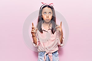 Beautiful child girl wearing casual clothes pointing up looking sad and upset, indicating direction with fingers, unhappy and