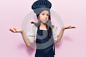 Beautiful child girl wearing cooker uniform clueless and confused with open arms, no idea and doubtful face