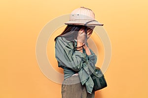 Beautiful child girl wearing explorer hat with sad expression covering face with hands while crying