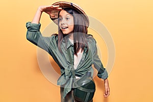 Beautiful child girl wearing explorer hat very happy and smiling looking far away with hand over head