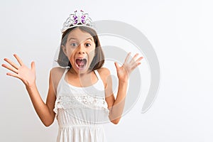 Beautiful child girl wearing princess crown standing over isolated white background celebrating crazy and amazed for success with