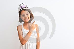 Beautiful child girl wearing princess crown standing over isolated white background cheerful with a smile of face pointing with