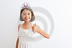 Beautiful child girl wearing princess crown standing over isolated white background doing happy thumbs up gesture with hand