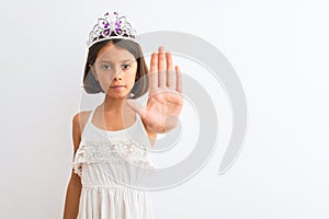 Beautiful child girl wearing princess crown standing over isolated white background doing stop sing with palm of the hand