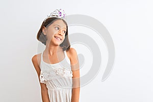 Beautiful child girl wearing princess crown standing over isolated white background looking away to side with smile on face,