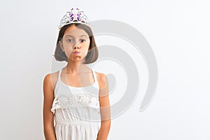 Beautiful child girl wearing princess crown standing over isolated white background puffing cheeks with funny face