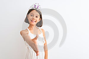 Beautiful child girl wearing princess crown standing over isolated white background smiling friendly offering handshake as