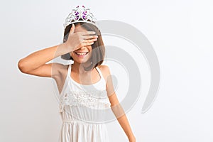 Beautiful child girl wearing princess crown standing over isolated white background smiling and laughing with hand on face