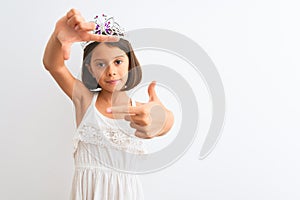 Beautiful child girl wearing princess crown standing over isolated white background smiling making frame with hands and fingers