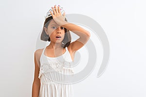 Beautiful child girl wearing princess crown standing over isolated white background surprised with hand on head for mistake,