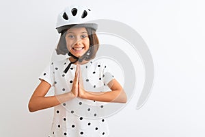 Beautiful child girl wearing security bike helmet standing over isolated white background praying with hands together asking for