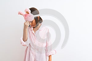 Beautiful child girl wearing sleep mask and pajama standing over isolated white background tired rubbing nose and eyes feeling