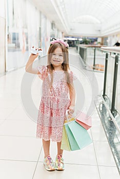 A beautiful child in the mall makes shopping. Online shopping concept. A girl in a pink dress with multi-colored pastel bags in