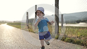 Beautiful child plays near the field in summer. A little boy running runs along the road.