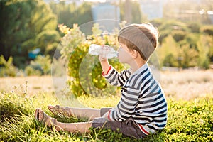 A beautiful child sitting on the grass drinks water from a bottle in the summer at sunset. Boy quenches his thirst on a hot day