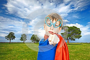 Beautiful child superhero standing on summer field background