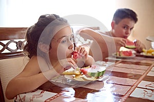 Beautiful children, brother and sister, boy and girl snack with ripe organic fresh and juicy watermelon in the kitchen.