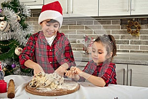 Beautiful children cooking together in the home kitchen during Christmas holidays. Adorable boy in Santa hat and his cute little