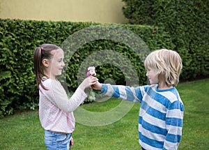 Beautiful children 6-7 years old in park, the boy gives the girl daisy flowers