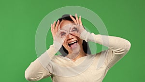 Beautiful chinese woman with happy face smiling making ok sign hand with eyes looking through fingers on green isolated