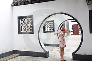 Beautiful Asian Chinese woman in traditional chi-pao cheongsam play violin in in a garden stand under arched door