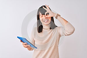 Beautiful chinese woman using blue tablet standing over isolated white background with happy face smiling doing ok sign with hand