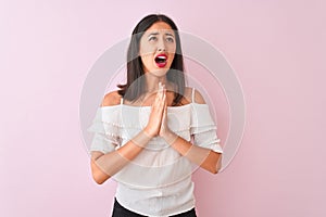 Beautiful chinese woman wearing white t-shirt standing over isolated pink background begging and praying with hands together with