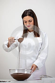 Beautiful chocolatier pouring dark melted chocolate isolated on white background