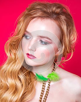 A beautiful choker made of gold chains and green fluff around the neck of a red-haired girl. Woman posing on red