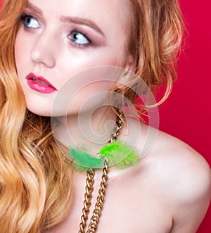 A beautiful choker made of gold chains and green fluff around the neck of a red-haired girl. Woman posing on red