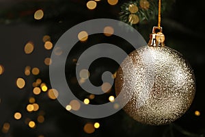 Beautiful Christmas ball hanging on fir tree branch against blurred lights, closeup. Space for text
