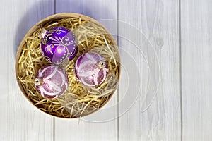 Beautiful Christmas balls with patterns in a wooden basket with a straw on a light wooden background  close up