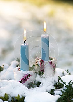 Beautiful Christmas candle holders made of ice, pink calluna blossom branches with burning blue candles in the snow covered garen.