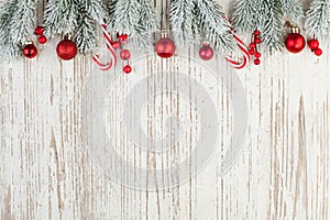 Beautiful Christmas composition border on white wooden background. Red holly berries, baubles and green fir branch. Minimal Xmas