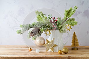 Beautiful Christmas decoration with pine tree branches in vase  and golden ornaments on wooden table over bright background