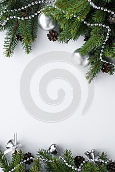 Beautiful christmas decoration in silver and green. Copy space surrounded by green spruce branches, cones, baubles, bells and